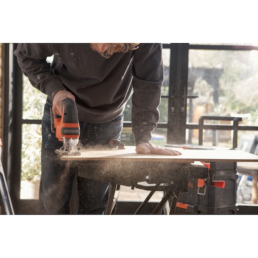 BLACKDECKER BLCJS78N jigsaw cutting wood on workbench with sawdust in workshop setting.