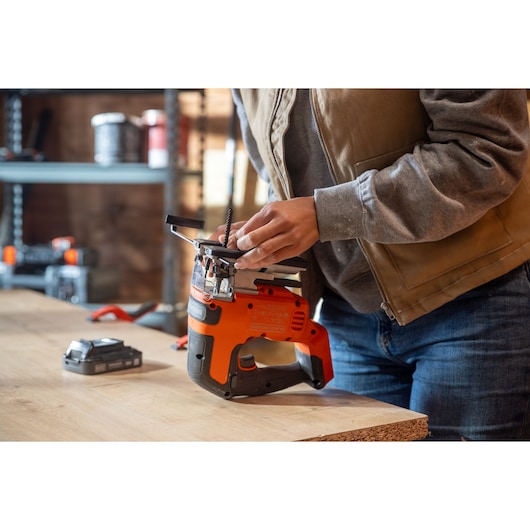 Photo of a person adjusting a BLACKDECKER jigsaw BLCJS78N on a workbench in a workshop setting.