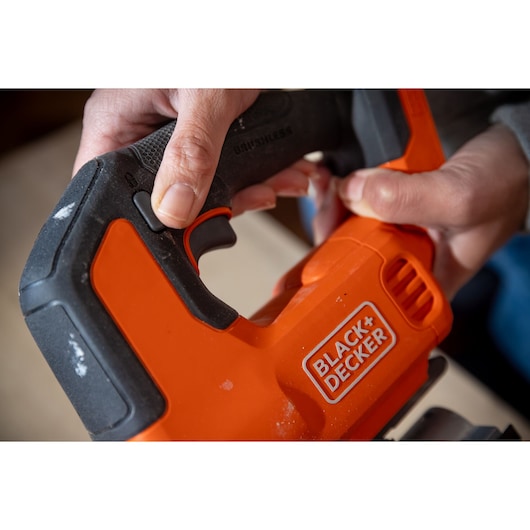 Close-up photo of BLACK+DECKER BLCJS78N jigsaw handle held by hands, showing orange and black grip detail.