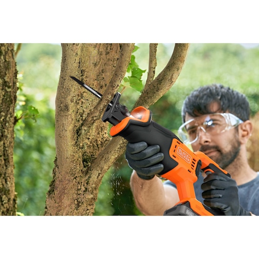 BLACKDECKER BLCR78N reciprocating saw cutting tree branch outdoors, close-up with hands in gloves.