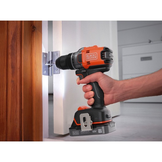 Photo of BLACK+DECKER BLD682D1 cordless drill driver in use securing a door hinge, orange and black design.