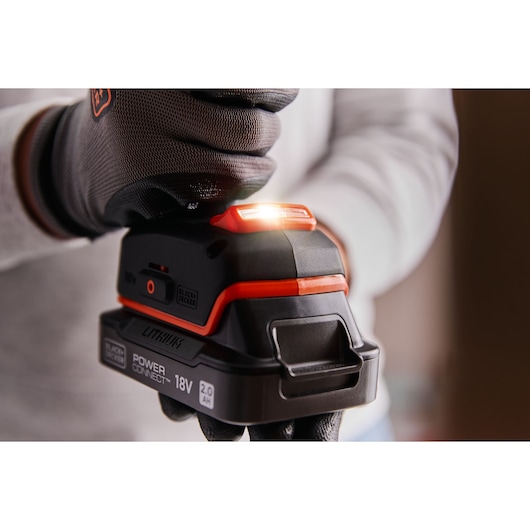 BLACK+DECKER BLD682D1 18V lithium-ion battery held by gloved hand, close-up with LED indicator light on.