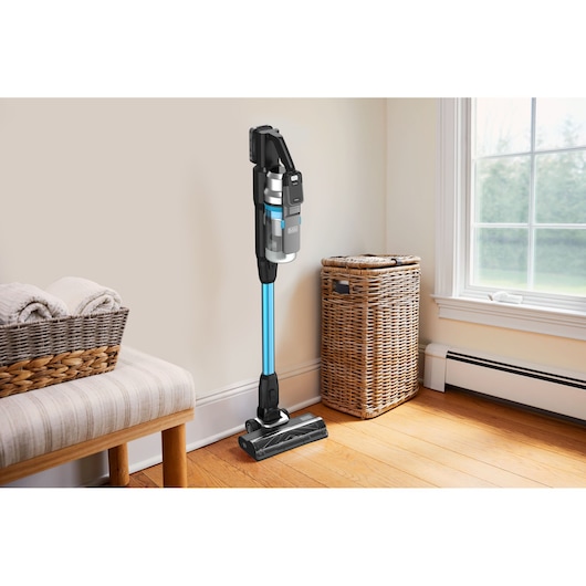 BLACKDECKER BSV520BRB cordless stick vacuum cleaner with blue wand, shown upright in a bright corner of a room.