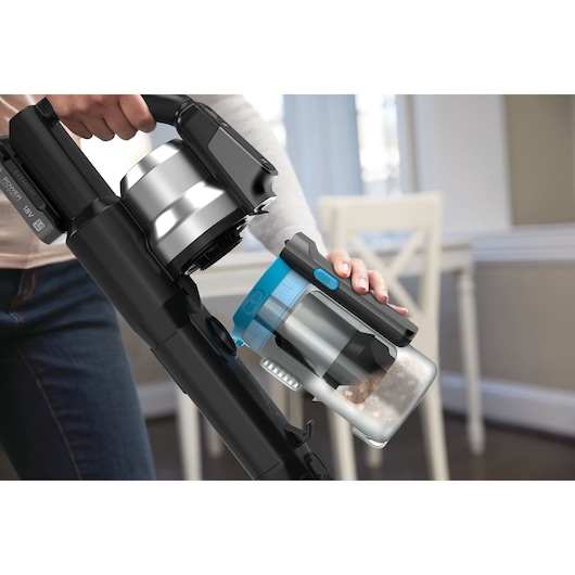 BLACK+DECKER cordless stick vacuum BSV520BRB with detachable dustbin, shown during cleaning in a home setting.