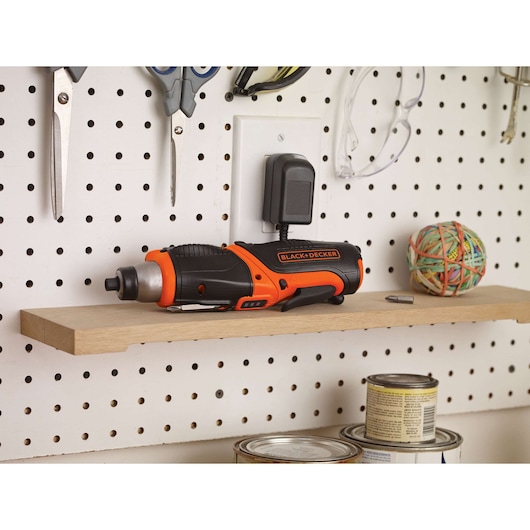 BLACK+DECKER CS3653LC cordless screwdriver, black and orange, side view on shelf in workshop setting.