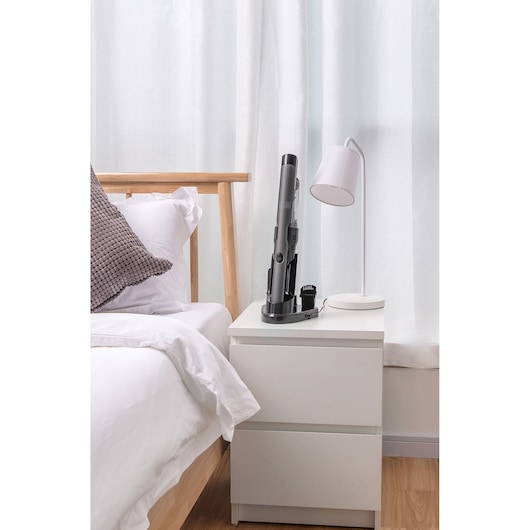 BLACKDECKER DVC320B21 cordless handheld vacuum on white nightstand next to modern lamp in bedroom.