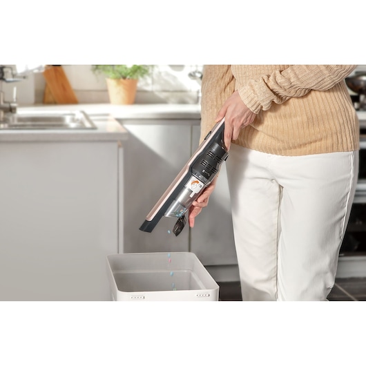 BLACKDECKER DVC320BRG handheld vacuum cleaner being emptied into a bin in a kitchen setting.