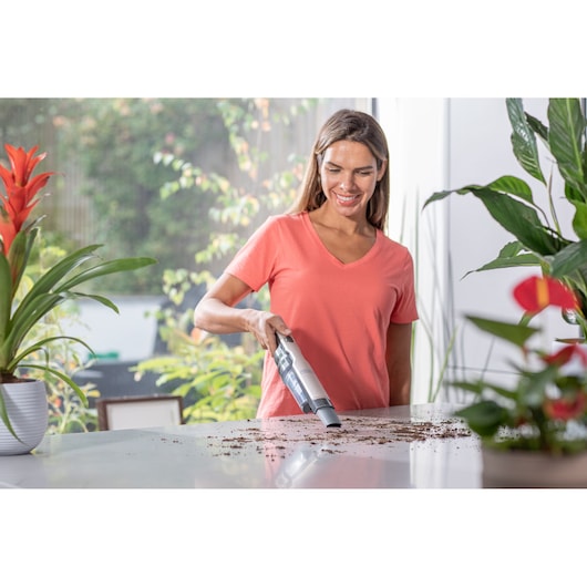 BLACKDECKER DVC320BRG handheld vacuum cleaning dirt on a white table with indoor plants.