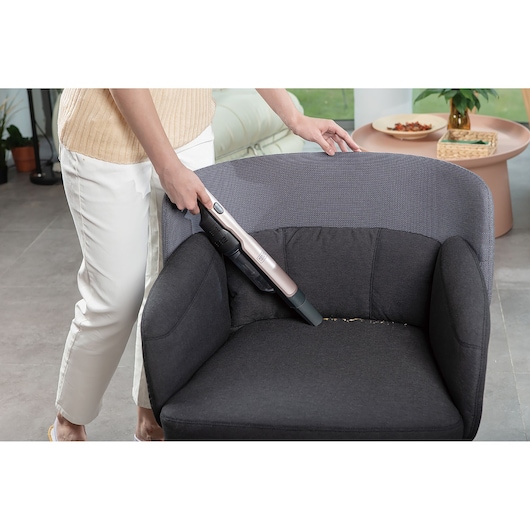 BLACKDECKER DVC320BRG handheld vacuum cleaning crumbs from a dark armchair in a living room scene.