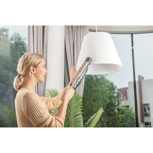 BLACK+DECKER DVC320BRG handheld vacuum used to clean a white lampshade in a modern living room.