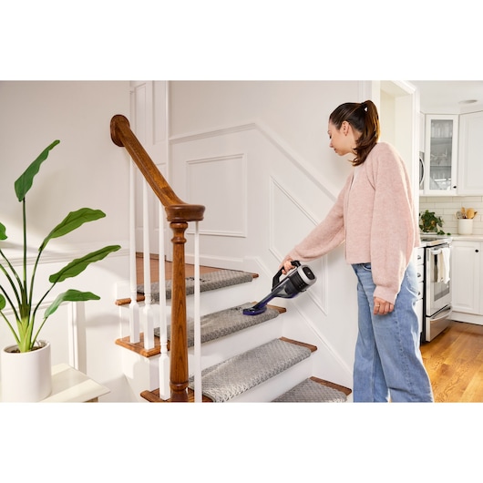 BLACK+DECKER DVD320BP handheld vacuum cleaning carpeted stairs in a home interior setting.