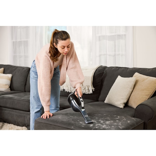 BLACKDECKER DVD320J handheld vacuum cleaning pet hair from a dark sofa in a living room.