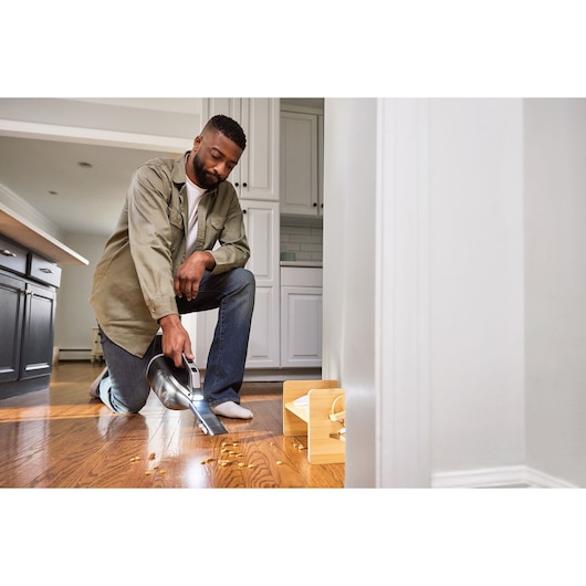 BLACKDECKER DVD320J handheld vacuum cleaning crumbs from a hardwood kitchen floor near a pet bowl.
