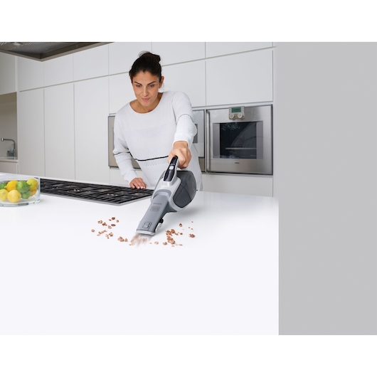 BLACKDECKER DVJ320JG handheld vacuum in use cleaning crumbs on white kitchen counter.