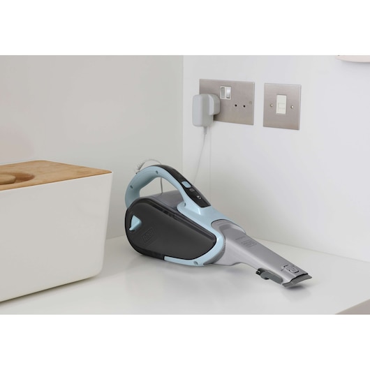 Photo of BLACK+DECKER DVJ325J handheld vacuum cleaner with light blue and black body charging on a kitchen counter.