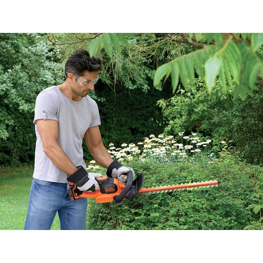 Photo of person trimming bushes with BLACK+DECKER hedge trimmer GTC18452PCB in a garden.