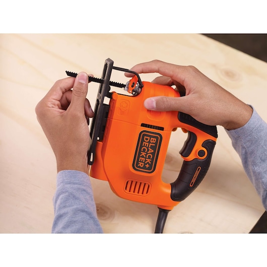 Photo of BLACKDECKER KS701E jigsaw being adjusted, orange and black body held by hands on wooden surface.