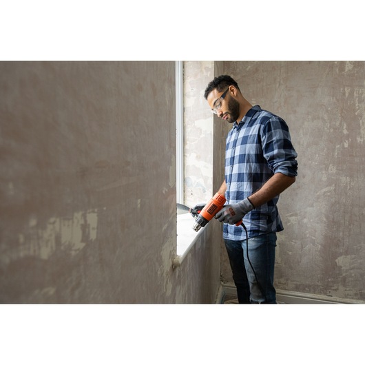 Photo of BLACKDECKER KX1650A heat gun used for window renovation, held by person in gloves and plaid shirt.