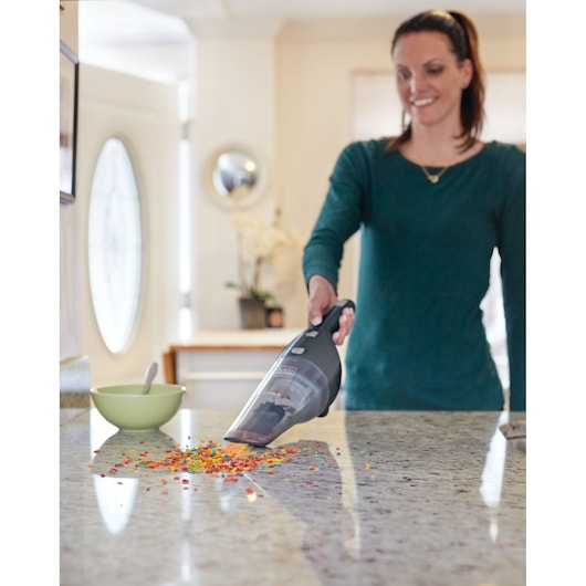 BLACKDECKER NSVA315J handheld vacuum cleaning colorful crumbs from kitchen counter near green bowl.
