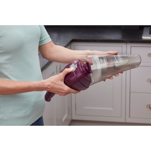 BLACKDECKER NVC115W handheld vacuum cleaner in purple held by a person in a kitchen, showing dustbin removal.