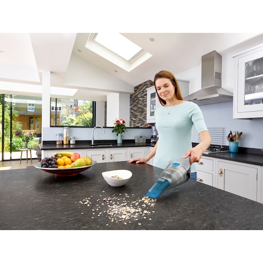 BLACK+DECKER NVC215WA handheld vacuum cleaning oats on kitchen counter near fruit bowl and cereal bowl.