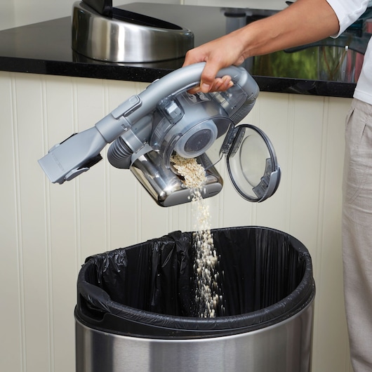 BLACKDECKER PD1820L handheld vacuum releasing debris into metal trash can, side view.