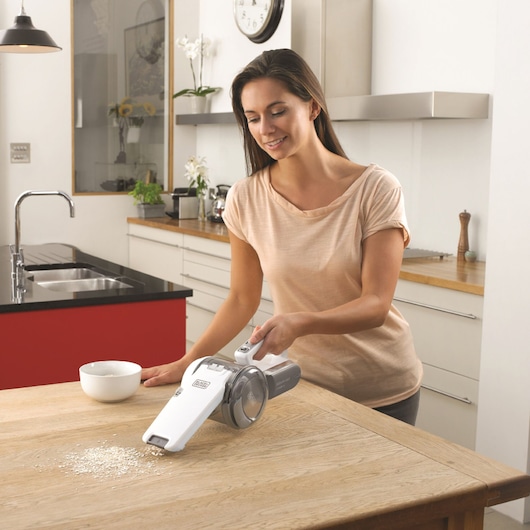 Photo of BLACKDECKER PV1820L handheld vacuum cleaning oats from a wooden kitchen table.