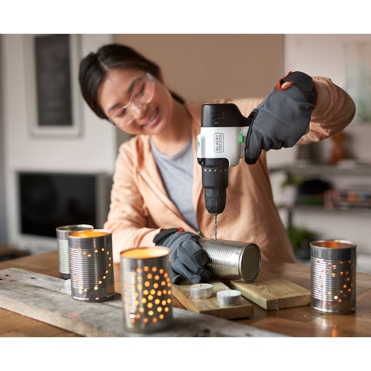 BLACKDECKER REVHD12C cordless drill used to make holes in a tin can, surrounded by lit DIY lanterns.