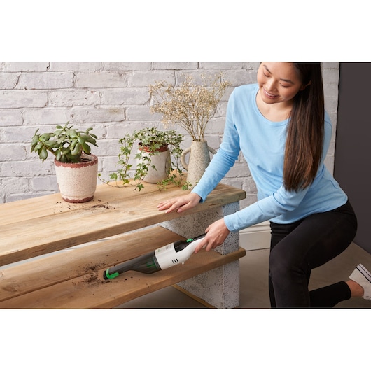BLACKDECKER REVHV8C handheld vacuum cleaning soil from wooden shelves near potted plants, indoor setting.