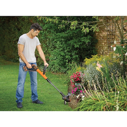 BLACKDECKER STC1840EPC garden trimmer used on lawn edge by flower bed outdoors.
