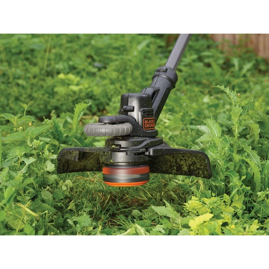 BLACK+DECKER STC1840EPC grass trimmer in use, cutting green weeds outdoors, close-up on cutting head.