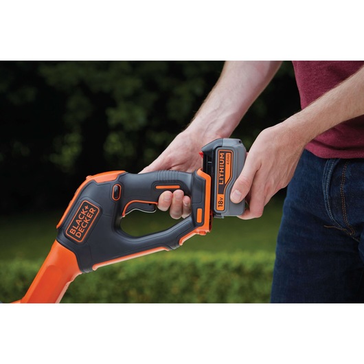 Photo of BLACK+DECKER STC1840EPC cordless grass trimmer, close-up of hands inserting 18V lithium battery.