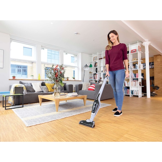 BLACKDECKER SVA320B cordless stick vacuum in use on wooden floor in modern living room.