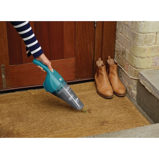 BLACKDECKER WDB115WA handheld vacuum in turquoise cleaning a doormat near brown boots, front view.