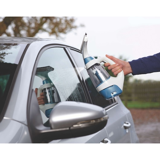BLACK+DECKER WW100 window cleaner spraying water on a car window outdoors.
