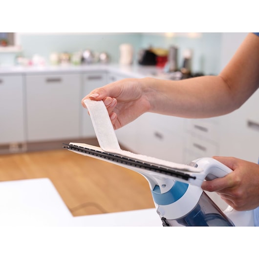 BLACKDECKER WW100 window cleaning tool with blue water tank held in hand, applying cleaning cloth in a kitchen.